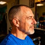 Homme de 55 ans avec coupe buzz courte portant une chemise bleue dans un barbershop éclairé naturellement