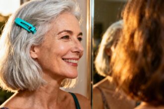 Femme aux cheveux argentés coiffés en carré avec un clip turquoise, souriant devant un miroir
