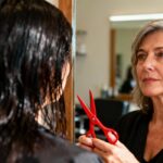 Femme de 55 ans dans un salon regardant pensivement son reflet dans un miroir avec des ciseaux rouges à la main